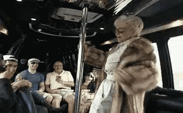 a group of people are riding on a bus with an elderly woman standing in front of them
