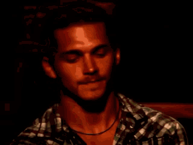 a man wearing a plaid shirt and a necklace looks up
