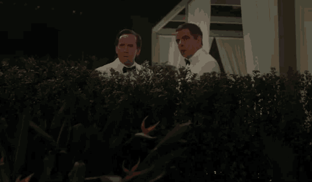 two men in tuxedos standing next to each other in front of a building