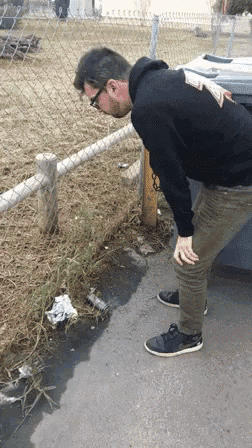 a man in a black hoodie is looking at a puddle of water