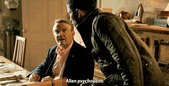 a man sitting at a table talking to another man who is standing next to him and says alien psychopath