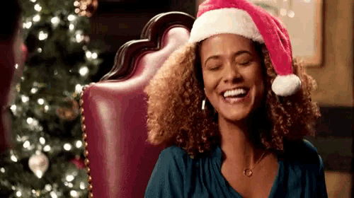 a woman is wearing a santa hat and smiling while sitting in front of a christmas tree .