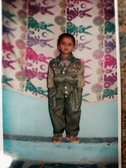 a young boy wearing a super jacket stands in front of a colorful wall