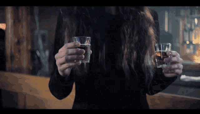 a woman in a black dress holds two shot glasses in her hands