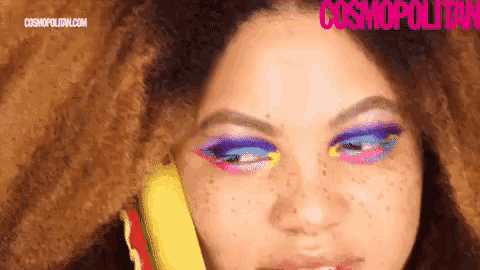 a close up of a woman 's face with colorful eye shadow and freckles talking on a phone .