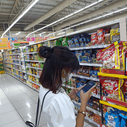 a woman wearing a mask looks at her phone in a grocery store aisle