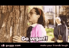 a girl standing next to a tree with the words go vegan on it