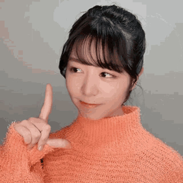 a woman wearing an orange sweater is holding her finger to her mouth
