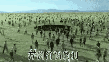 a large group of people are walking in a field with mountains in the background .