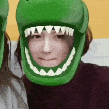 a woman wearing a green dinosaur mask with sharp teeth is smiling .