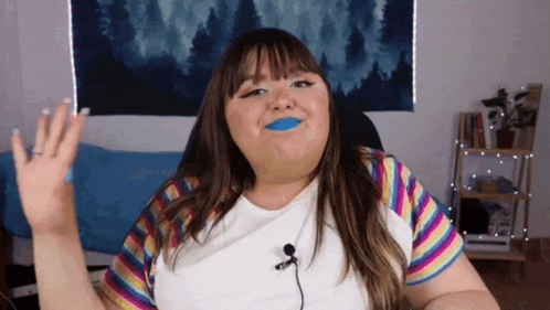 a woman with blue lipstick is sitting in front of a microphone and waving her hand .