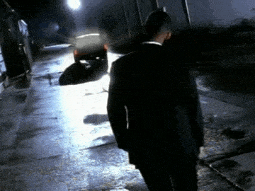a man in a suit is walking down a dark alleyway at night