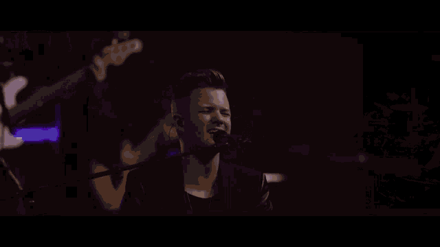 a man in a leather jacket is playing an electric guitar in a dark room