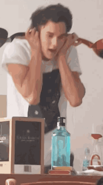 a man covering his ears with his hands in front of a bottle of gin baron