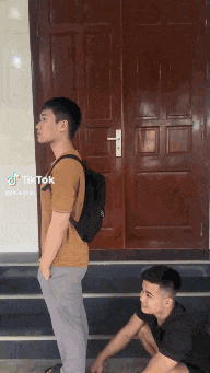 a man with a backpack is standing next to another man kneeling down .