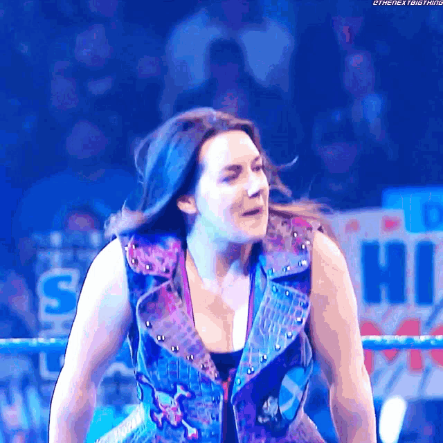 a woman is standing in a wrestling ring with a sign that says hi in the background