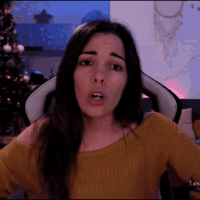 a woman in a yellow sweater is making a face in front of a christmas tree