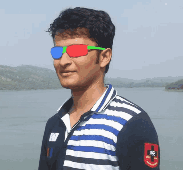 a man wearing 3d glasses and a striped shirt stands in front of a lake