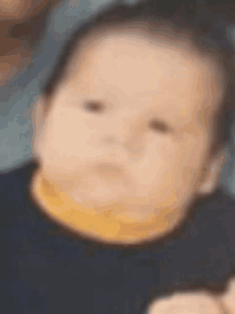 a baby is making a funny face and wearing a black shirt and a yellow collar .