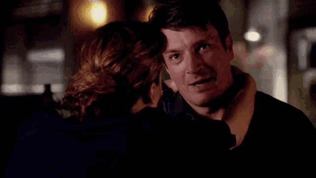 a man and a woman are looking at each other and the woman is holding the man 's neck