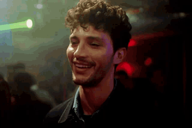 a man with curly hair is smiling in a club