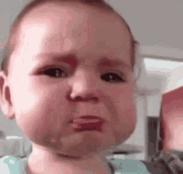 a baby is crying and making a funny face with his tongue out .