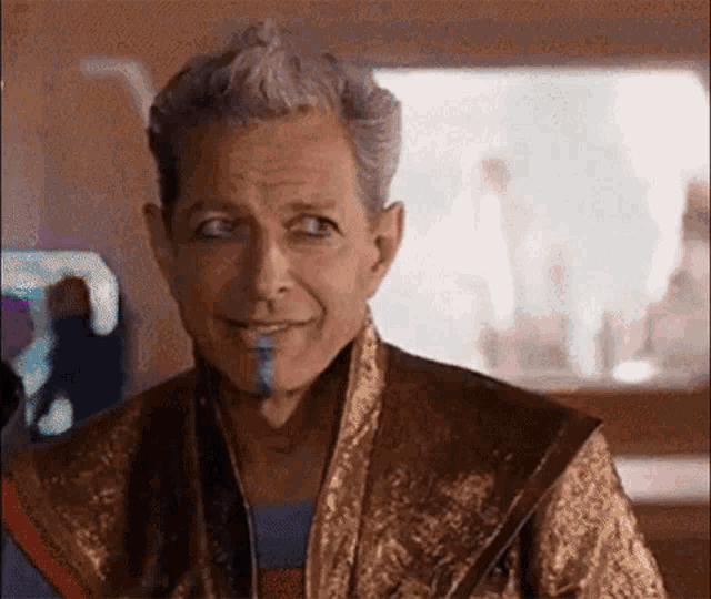 a man with gray hair and a blue beard is smiling while wearing a gold robe .