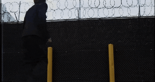a woman walks past a no parking sign on a barbed wire fence
