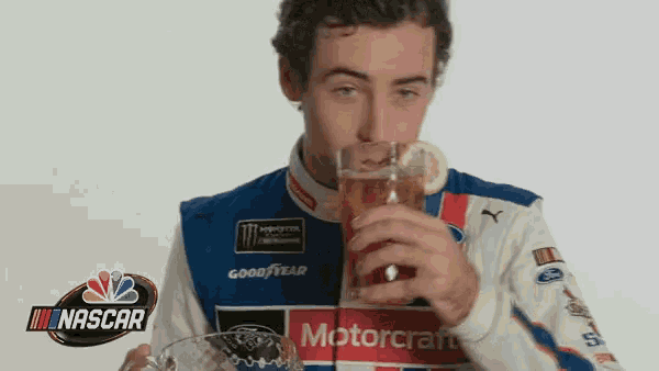 a man in a nascar uniform is drinking from a glass with a lemon slice on it .