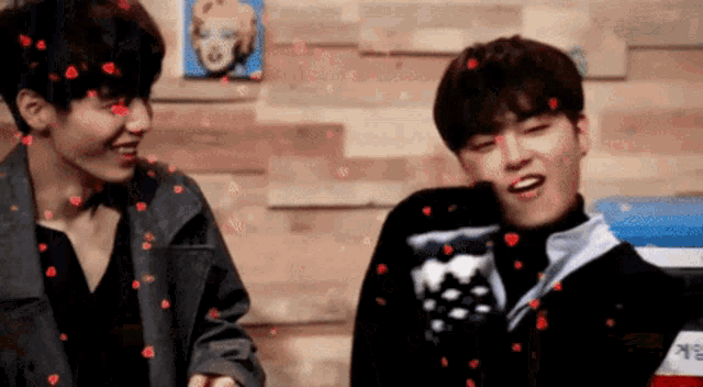 two young men are standing next to each other and hearts are falling from the sky around them .