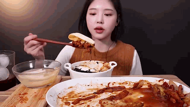 a woman is eating a plate of food with chopsticks and a bowl of sauce .