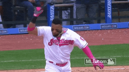 a baseball player wearing a white indians jersey and pink gloves is running on the field