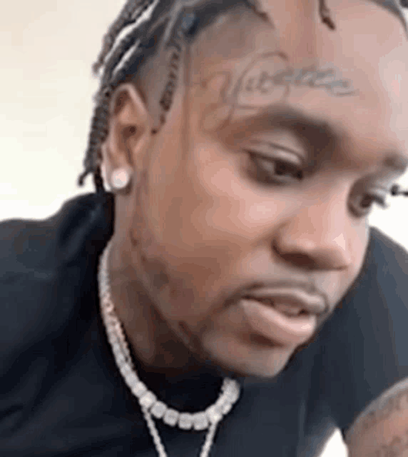 a man with dreadlocks and a tattoo on his forehead is wearing a necklace .