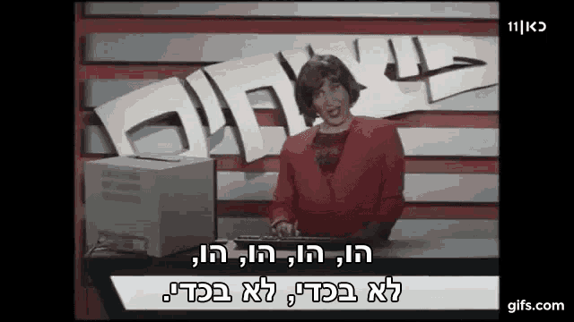 a woman in a red sweater is standing in front of a computer with hebrew writing on it .