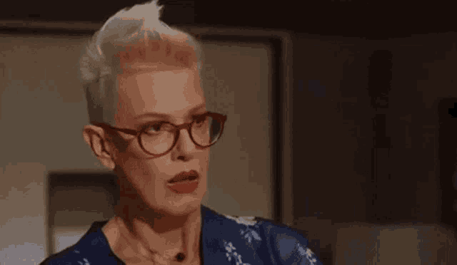 a woman with short blonde hair and red lipstick is wearing glasses and a blue dress .