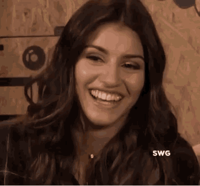 a woman with long hair is smiling and looking at the camera while standing in front of a wooden wall .