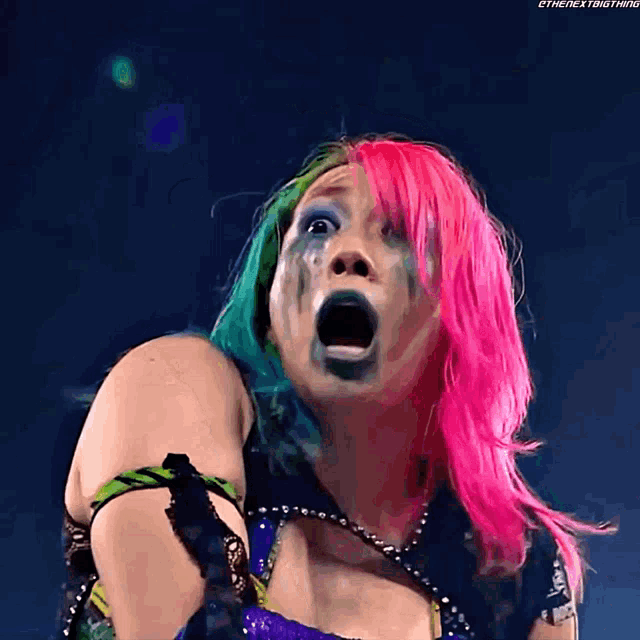 a woman with pink and green hair is making a funny face with her mouth open