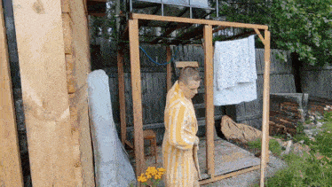 a man in a yellow and white striped robe stands in front of a wooden fence