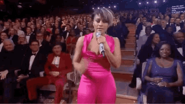a woman in a pink dress is standing in front of a microphone in front of a crowd .