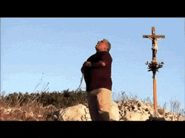 a man is praying in front of a cross with a statue of jesus on it