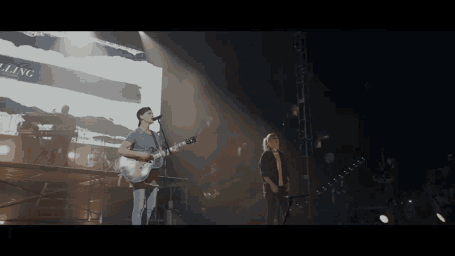 a man singing into a microphone while another man plays a guitar on stage