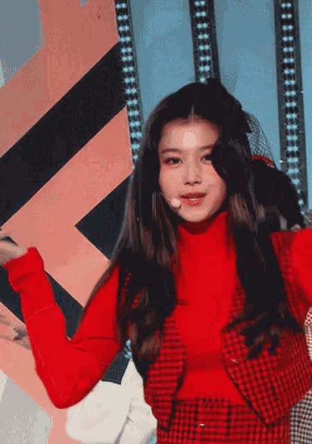 a woman in a red turtleneck and plaid vest is dancing on a stage