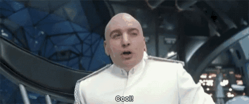a bald man in a white suit is standing in a room and saying cool .