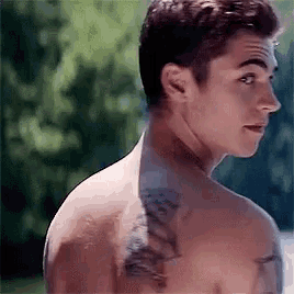 a shirtless man with a tattoo on his back is looking at the camera .