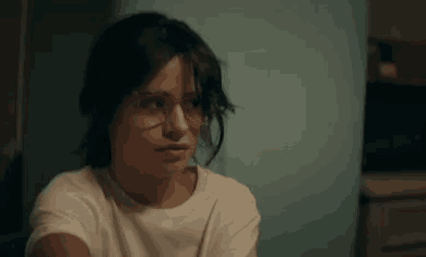 a woman wearing glasses and a white t-shirt is sitting in a room .
