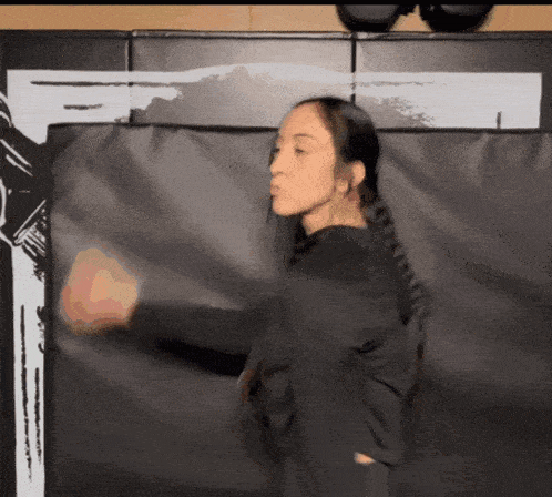 a woman in a black shirt stands in front of a black wall