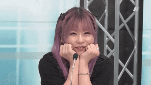 a girl with purple hair is smiling with her hands on her chin