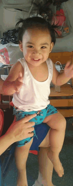 a little girl wearing a white tank top and blue shorts is sitting on a person 's lap