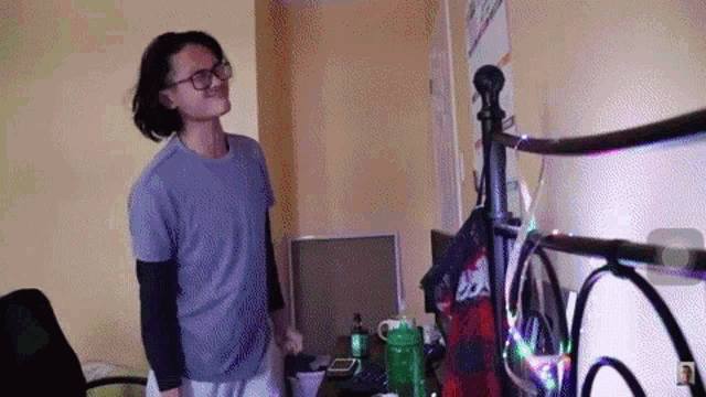 a man wearing glasses is standing in front of a bed in a bedroom .