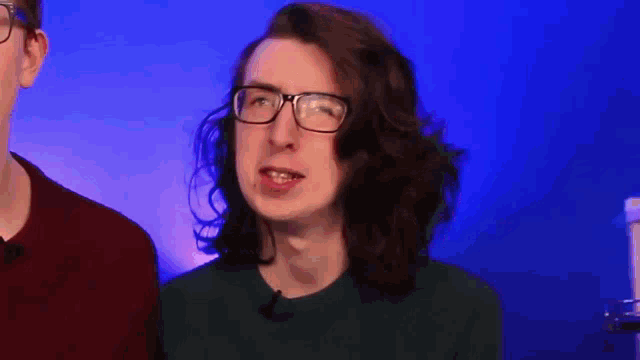 a man with long hair and glasses is making a funny face in front of a blue background .